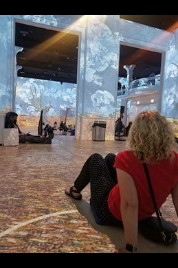 Lisa sitting on floor looking at paintings illuminated on the wall and floor