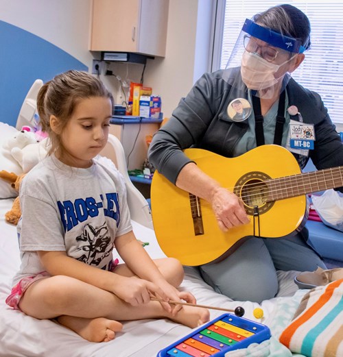 Child and music therapist in a hospital room. The music therapist, Jody, is playing guitar