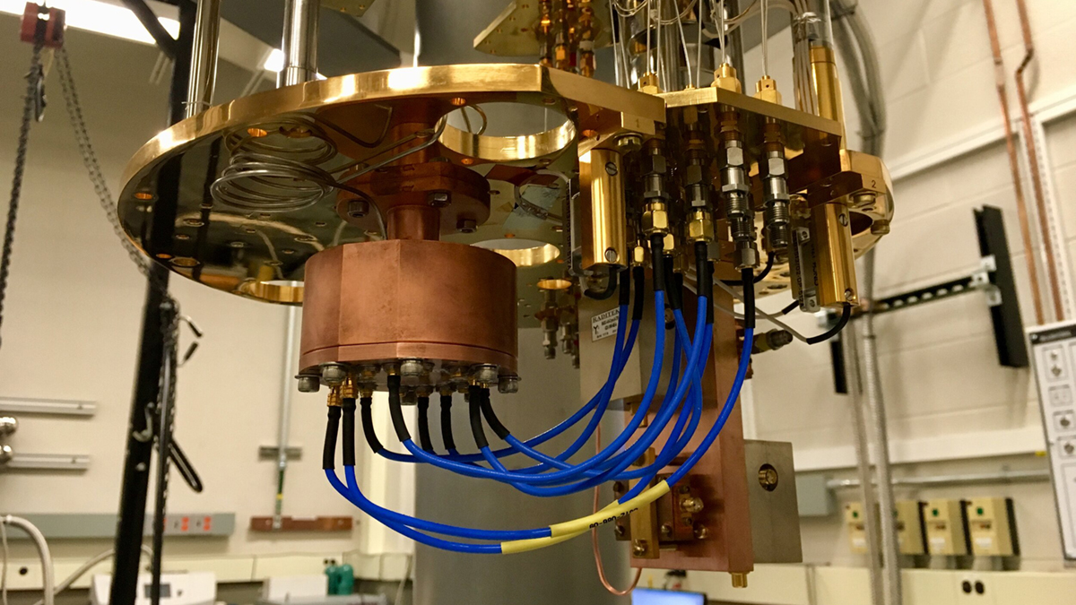 A photograph from inside an MSU lab shows an experimental set-up consisting of a golden metal base suspended from the ceiling. Attached to this base and hanging below it is a squat copper cylinder with several blue wires running out of it.