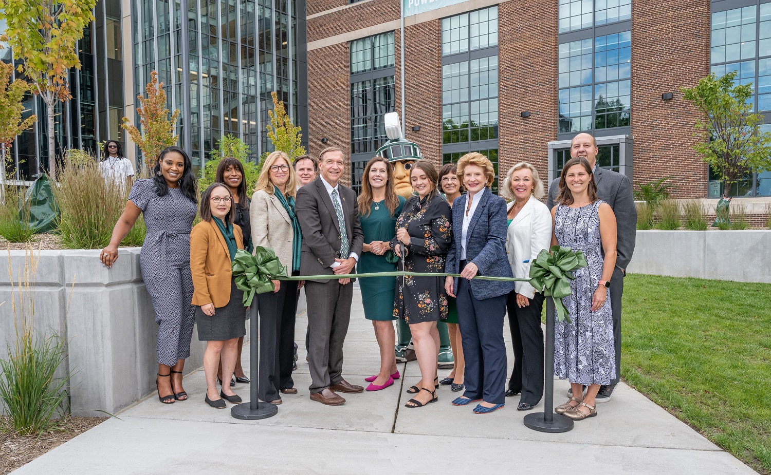 A group of people in front of the STEM Teaching and Learning Facility cutting a green ribbon. 