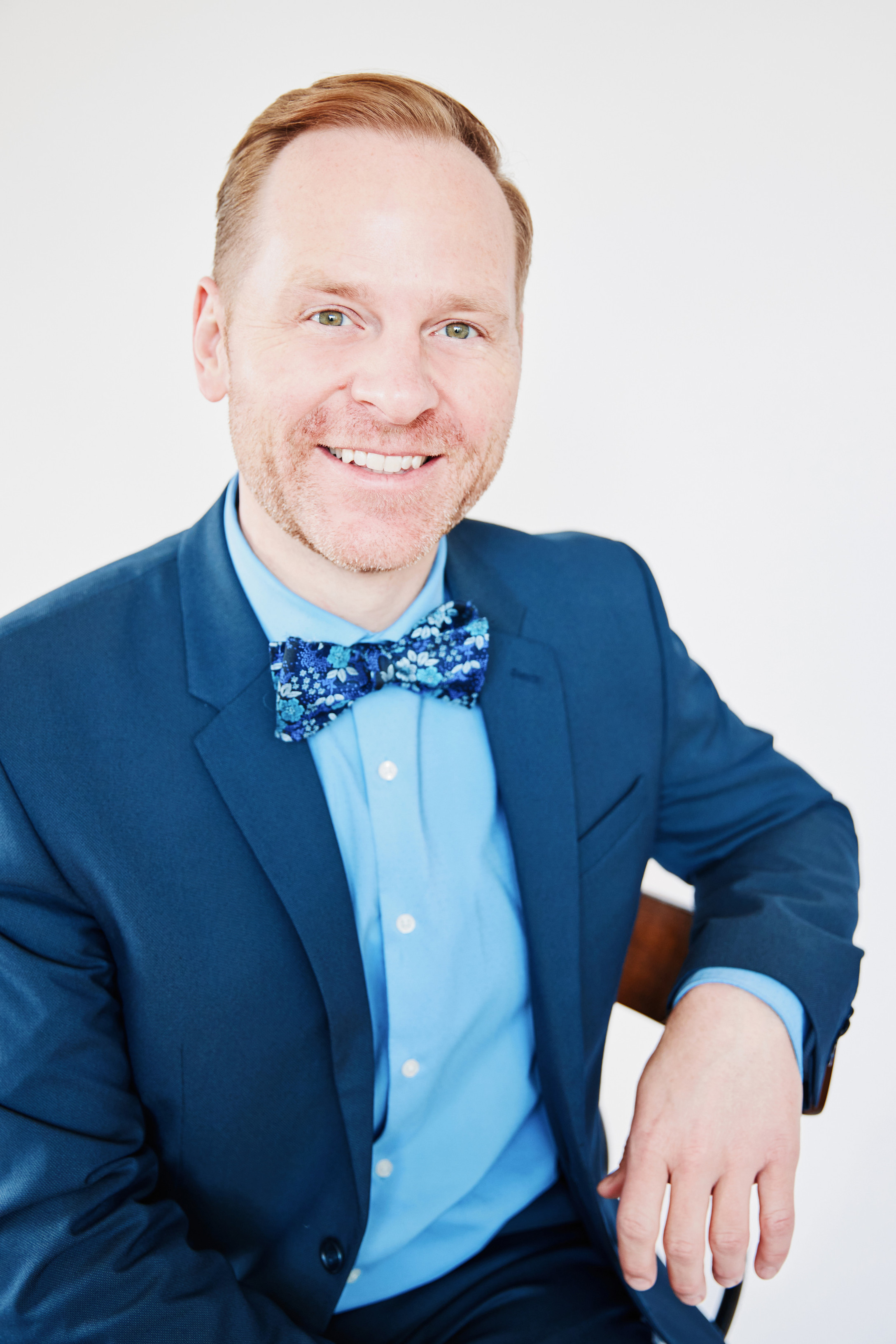 Photo of Eric Olmscheid in a blue suit jacket, blue shirt and blue bow tie