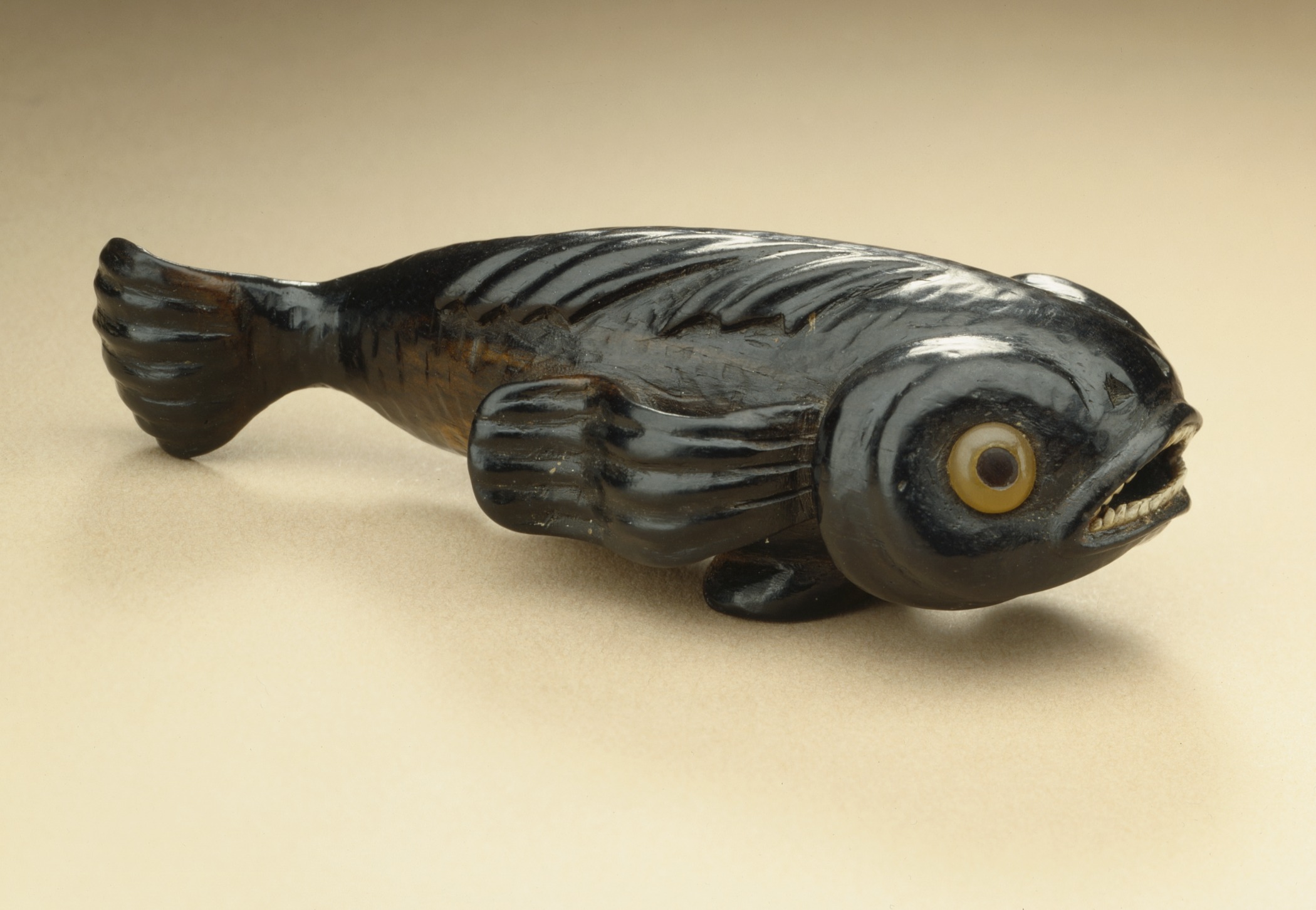 A carving of a carnivorous pilot fish made from black persimmon wood with colored inlays for its eyes (yellow) and teeth (white).