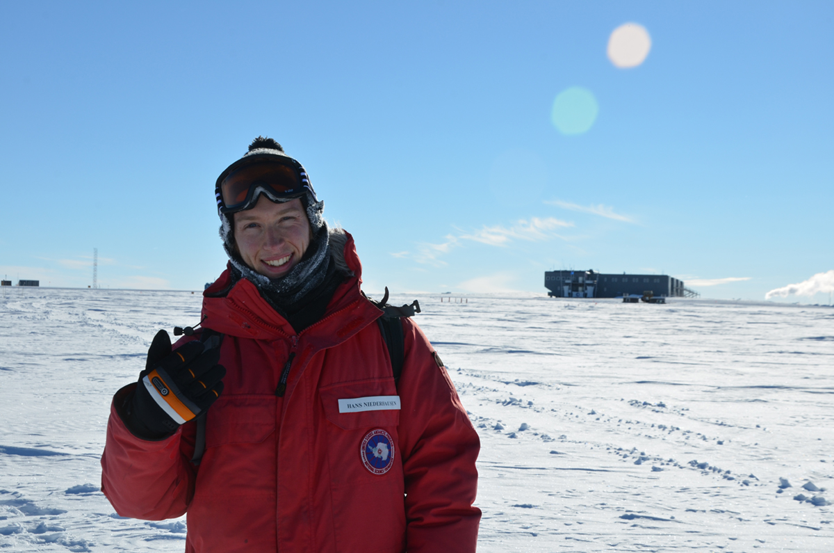 MSU postdoctoral research associate Hans Niederhausen in Antarctica. His red parka stands out against the white snow and clear blue sky.