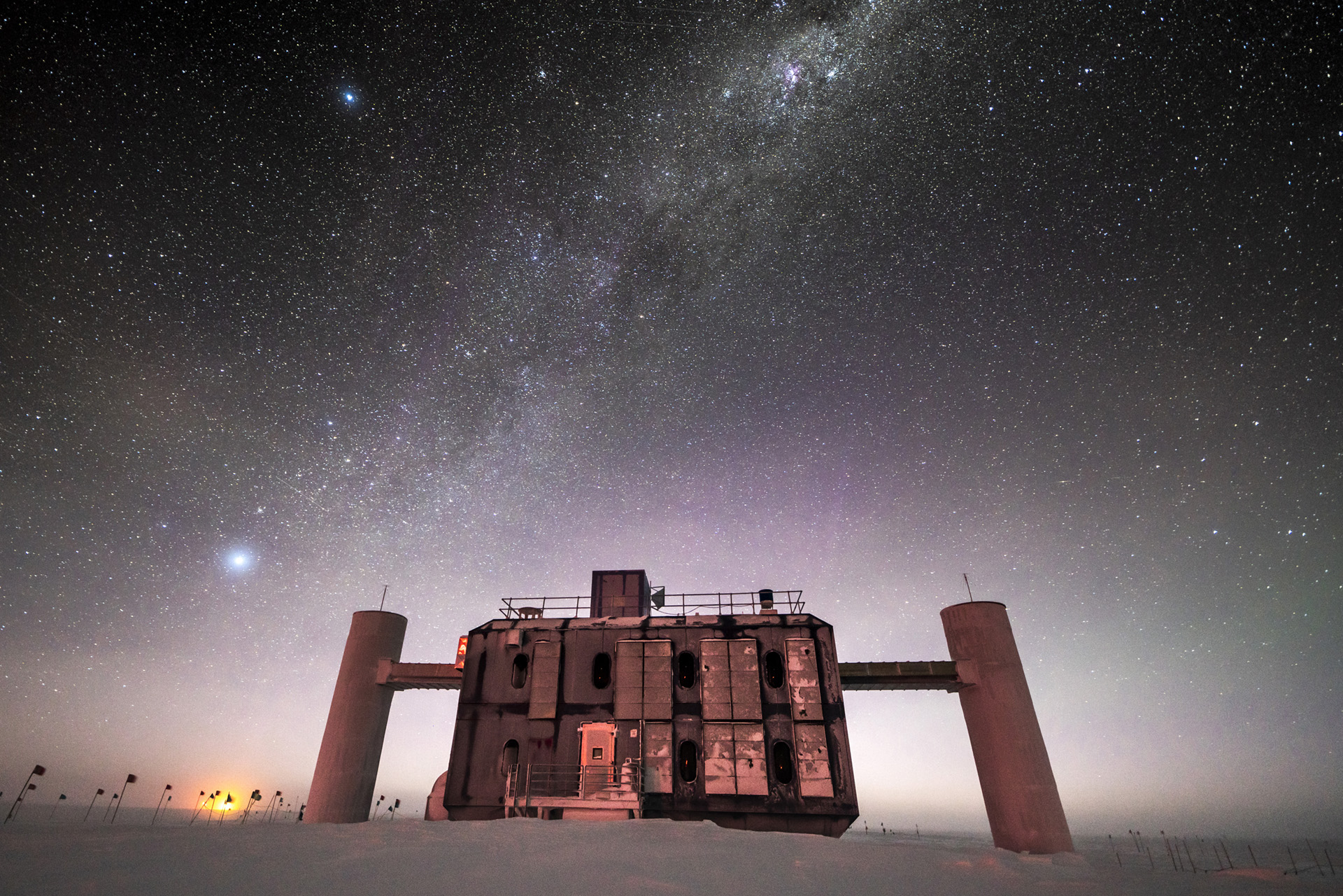 IceCube at twilight, with a starry sky showing a glimpse of the Milky Way overhead and sunlight lingering on the horizon.
