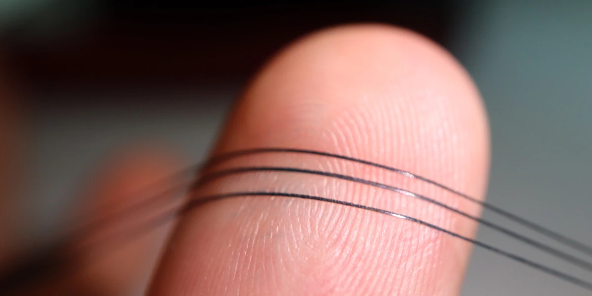 A photograph shows a close-up of three long, dark strands, which are NeuroString sensors, bending around a fingertip.