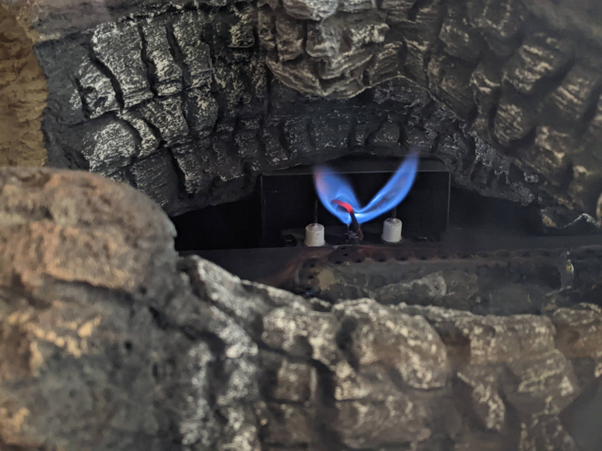 A small pilot light burns blue between faux logs in a gas fireplace.