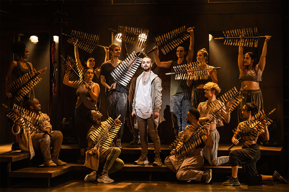 A man stands on a stage in the center of a group of people holding objects made to resemble leaves.