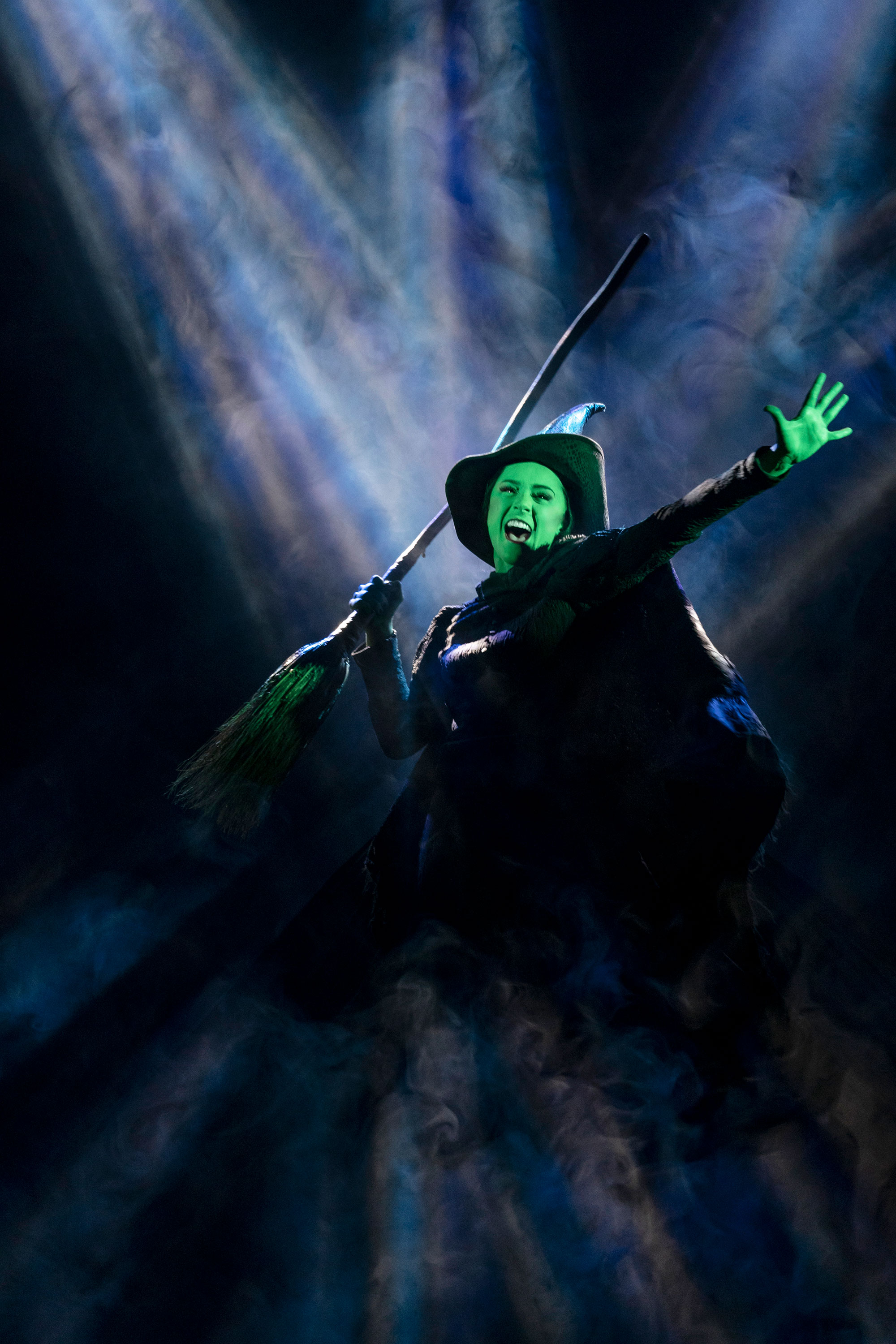 A woman dressed as a witch with a green face and hands holding a broom.