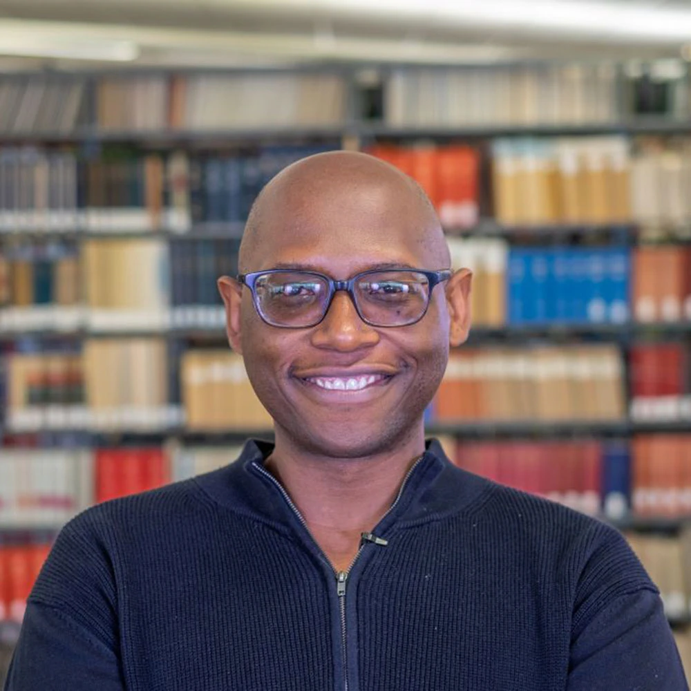 MSU Professor of English Julian Chambliss smiles in a portrait with books on bookshelves in the background. 