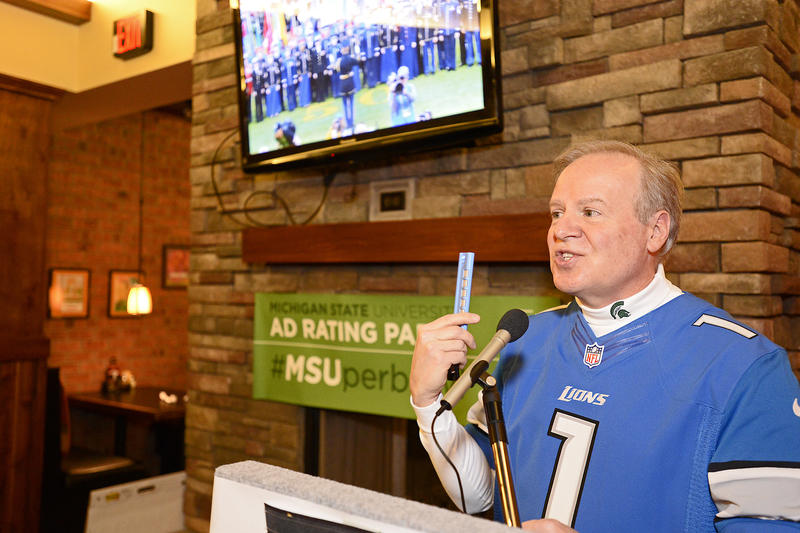Robert Kolt speaking at a podium during a Super Bowl ad ratings watch party.