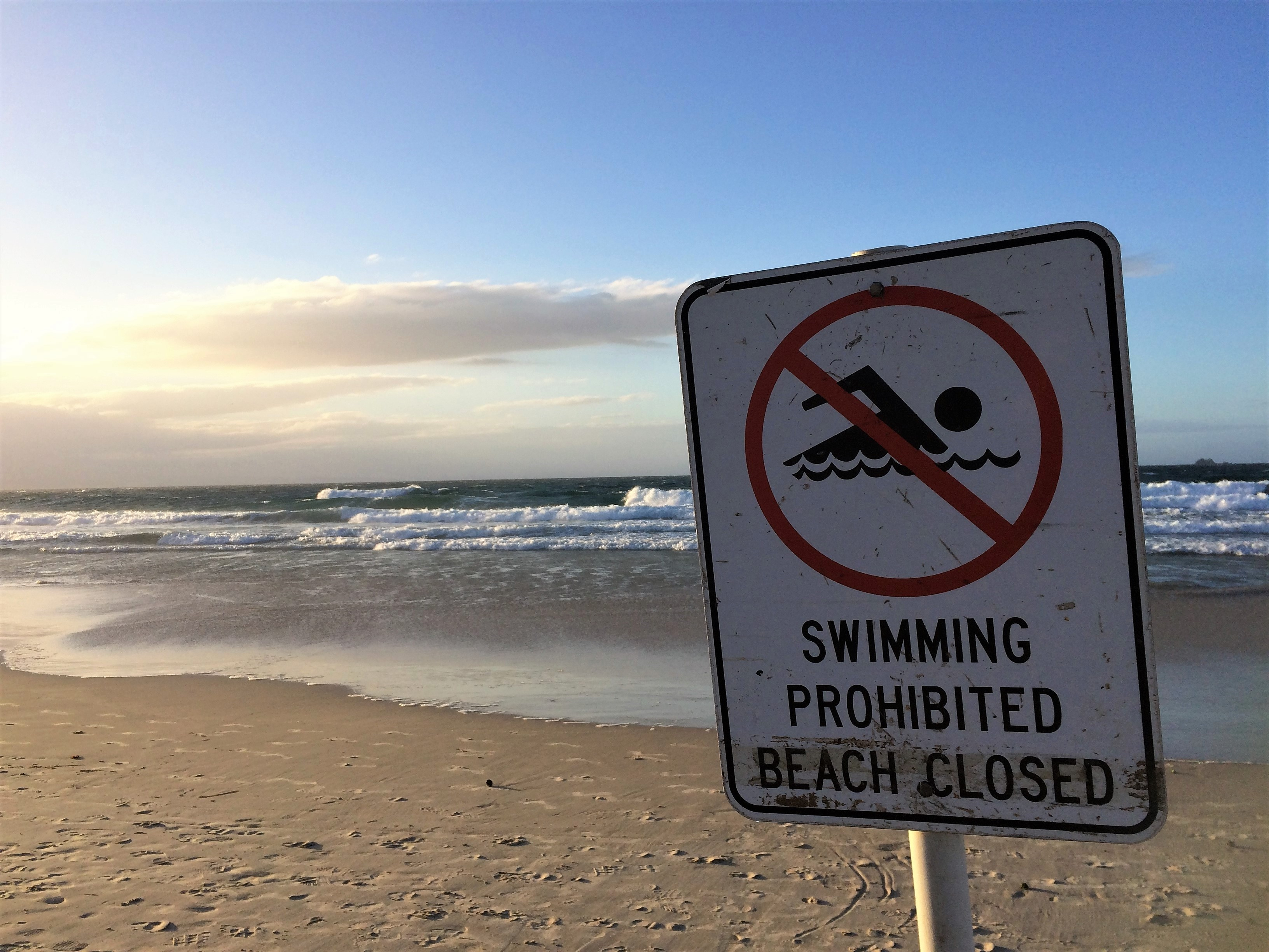 A no swimming sign in front of a beach and body of water