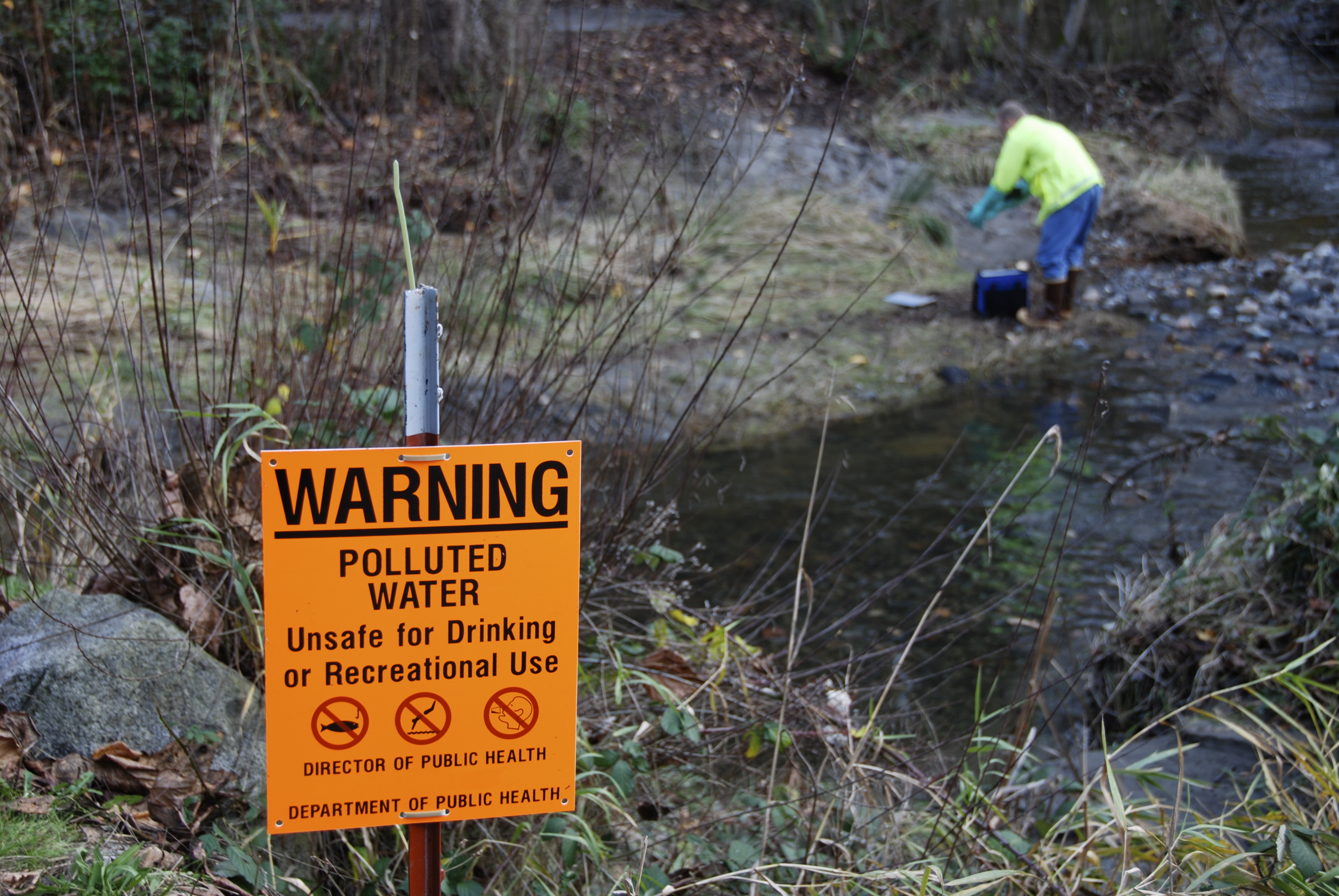 A person working in a river with a polluted water sign in the foreground
