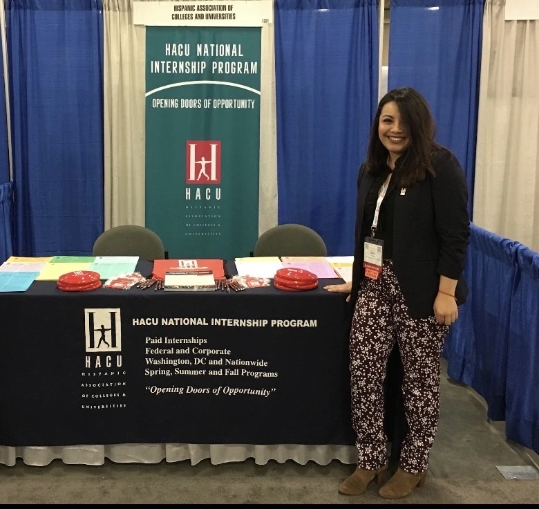Fabiola Yanez standing next to the Hispanic Association of Colleges and Universities National Internship Program table