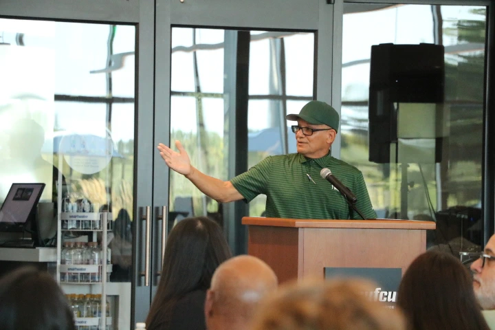 Luis Alonzo Garcia motions to his left while speaking at the lectern in front of a seated group