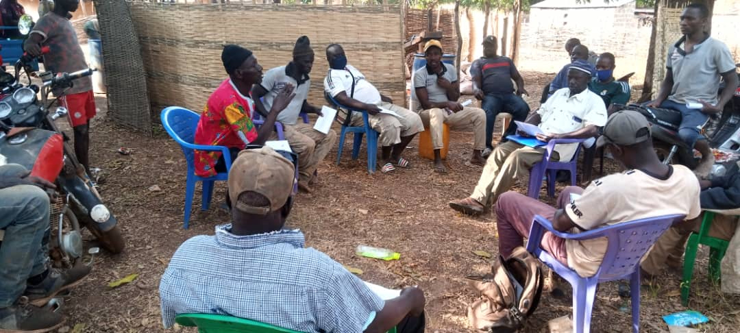 A group of people sitting in a circle on plastic chairs are having a discussion.