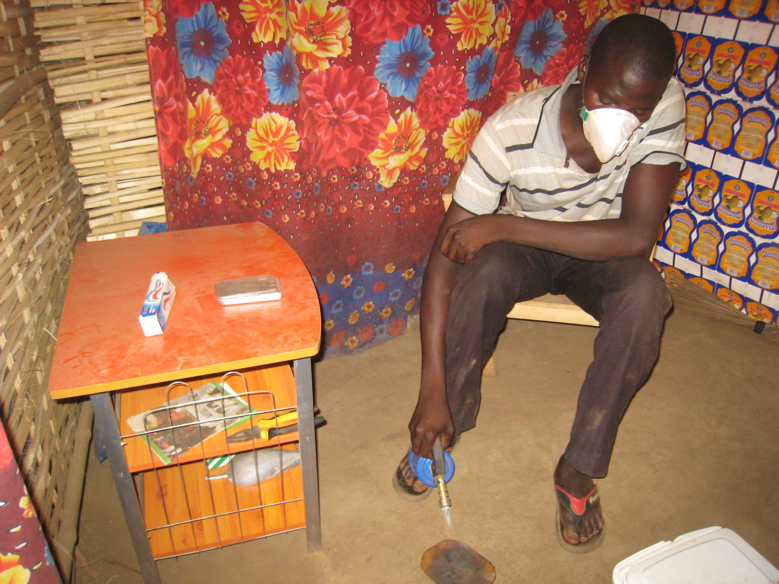 An artisanal gold miner burns mercury off a gold-mercury amalgam using a blow torch on the floor of a hut.
