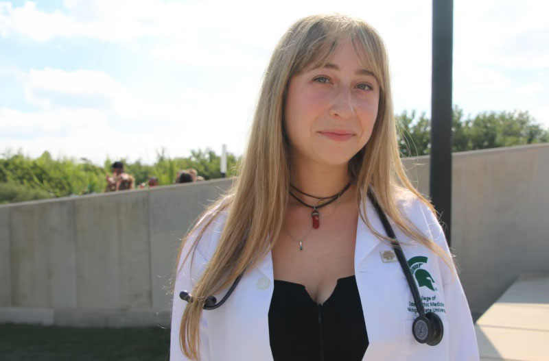 Paige Stern, a medical student wears a white coat with a stethoscope hanging from her shoulders