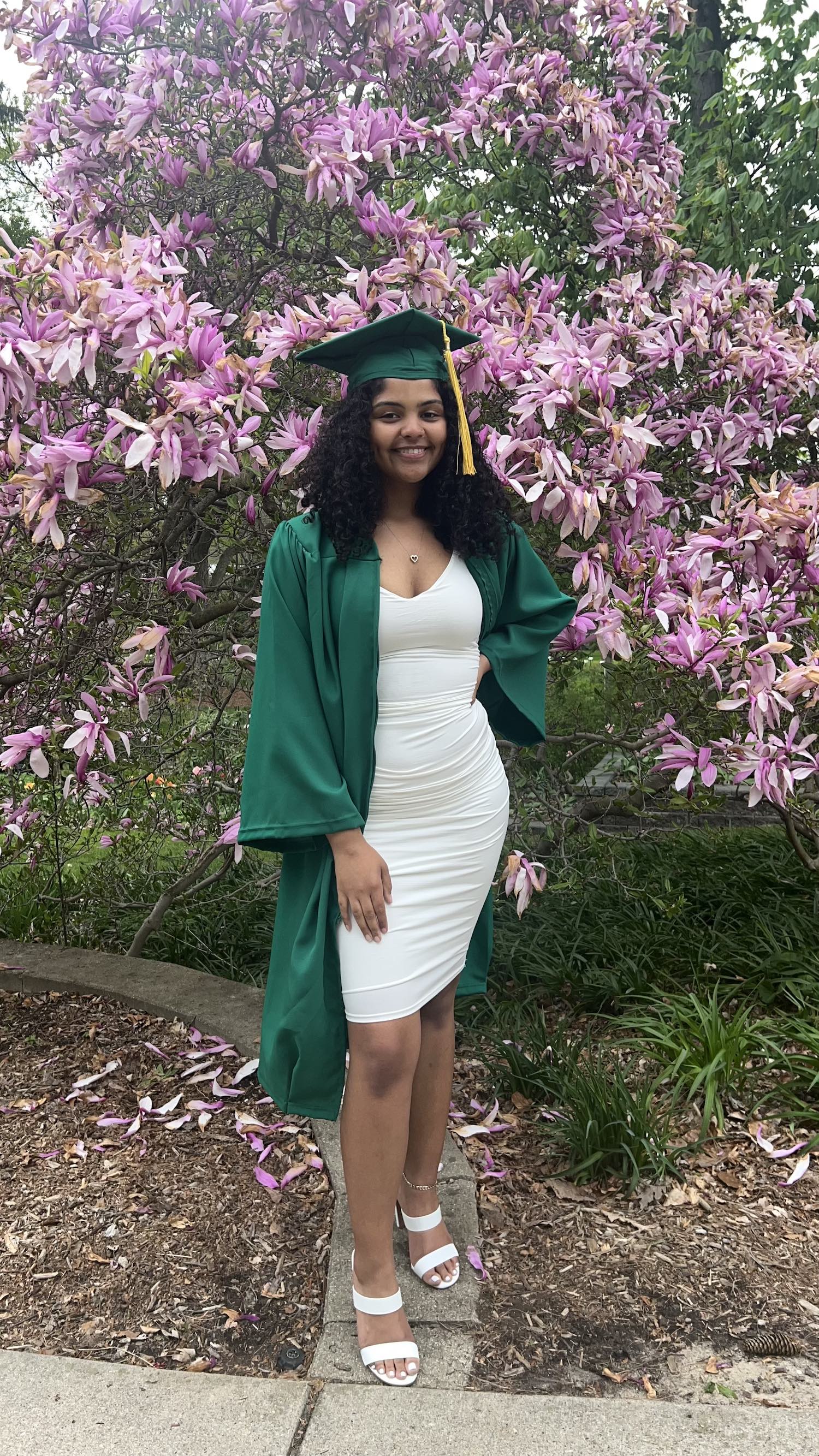 MSU graduate Angelica Bajos in a cap and gown in front of a blooming tree