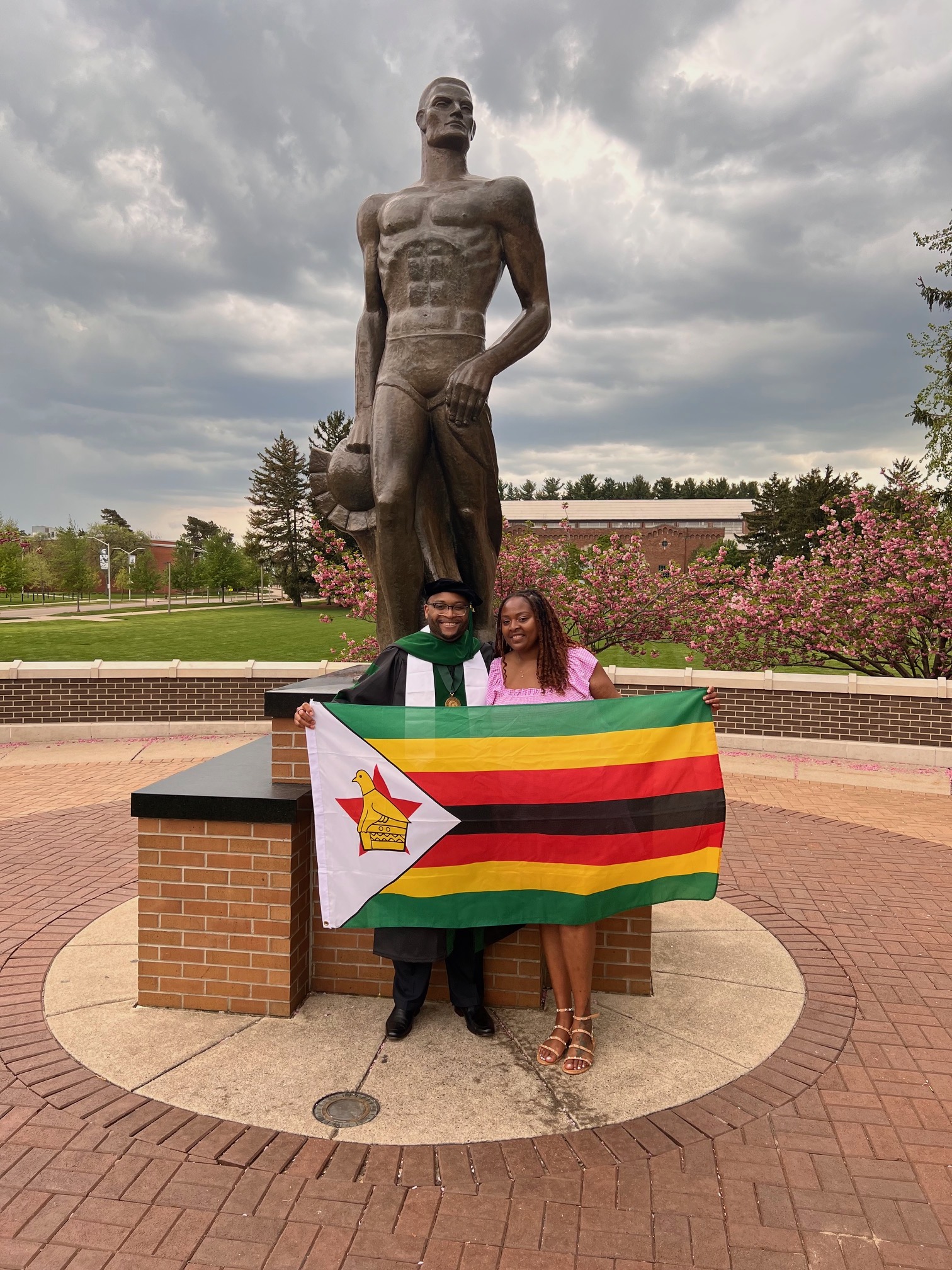 Michael Nyika Andrew poses in front of The Spartan statue with his sister, as they both hold the flag of Zimbabwe