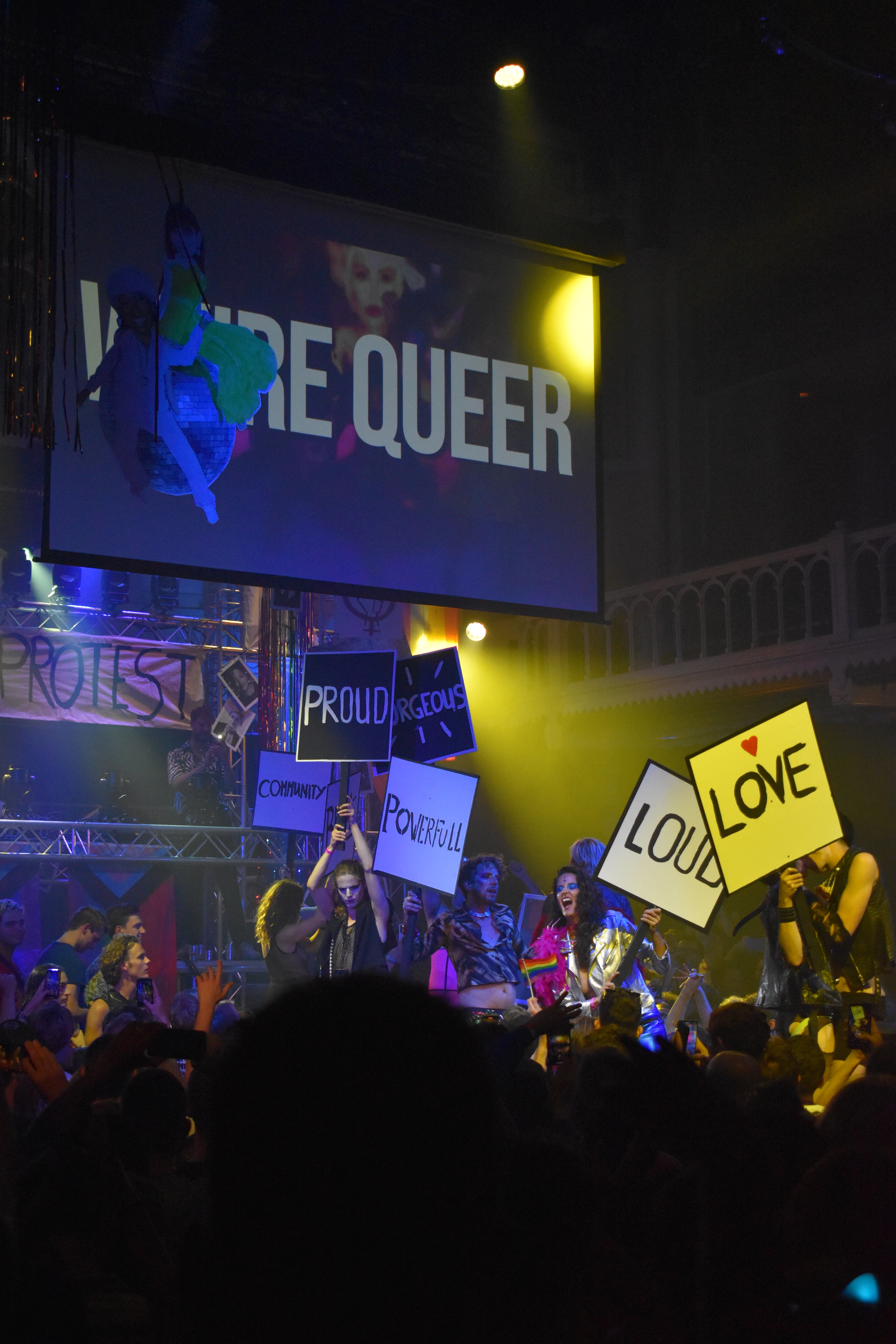 a concert during Amsterdam's Canal Pride festival at the historic Paradiso concert hall, with signs celebrating queer identities, love, and pride.