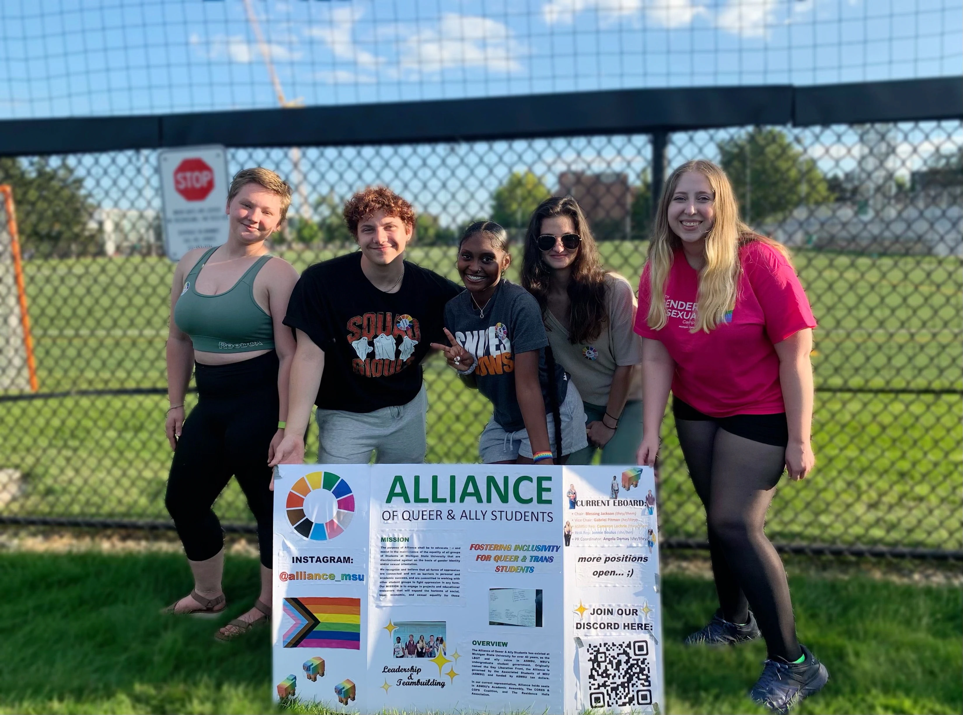 Group of students pose for an outdoor photo with a poster presentation board of The Alliance of Queer and Ally Students