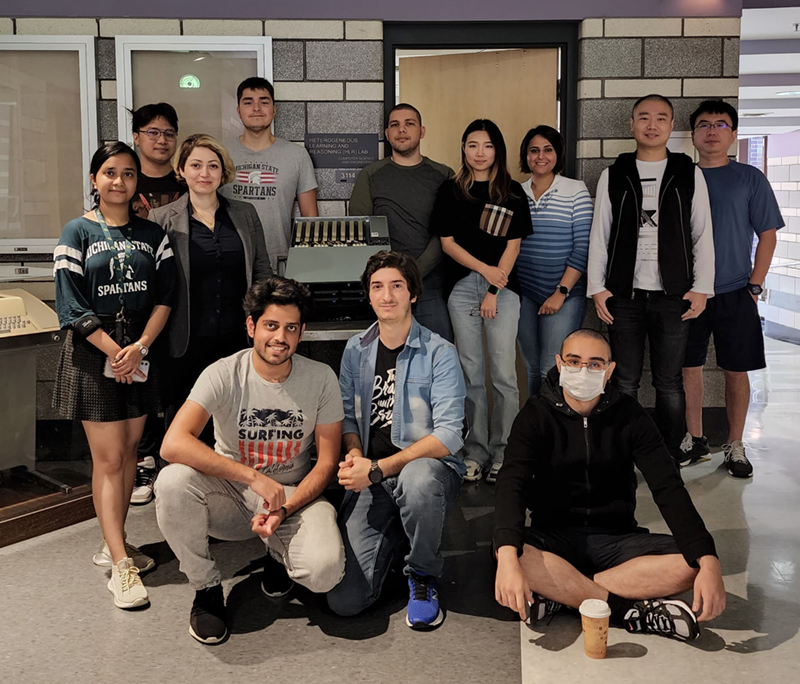 Assistant Professor Parisa Kordjamshidi stands with her team in front of the doorway to the Heterogeneous Learning Lab at Michigan State University.