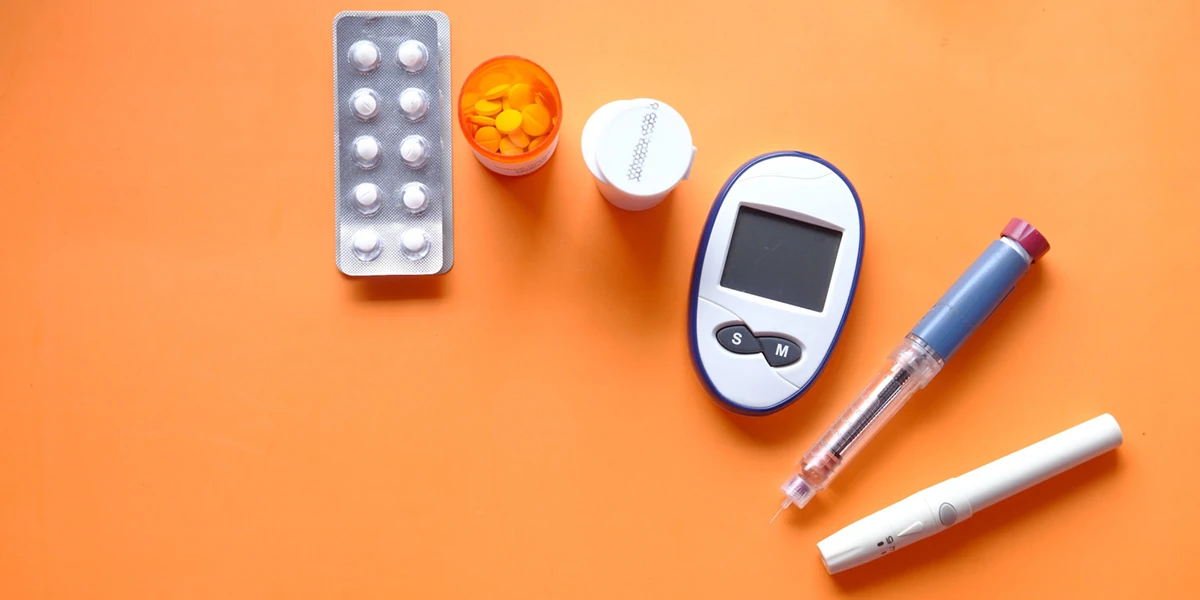 Pills, an insulin pen and a blood sugar monitor on an orange background