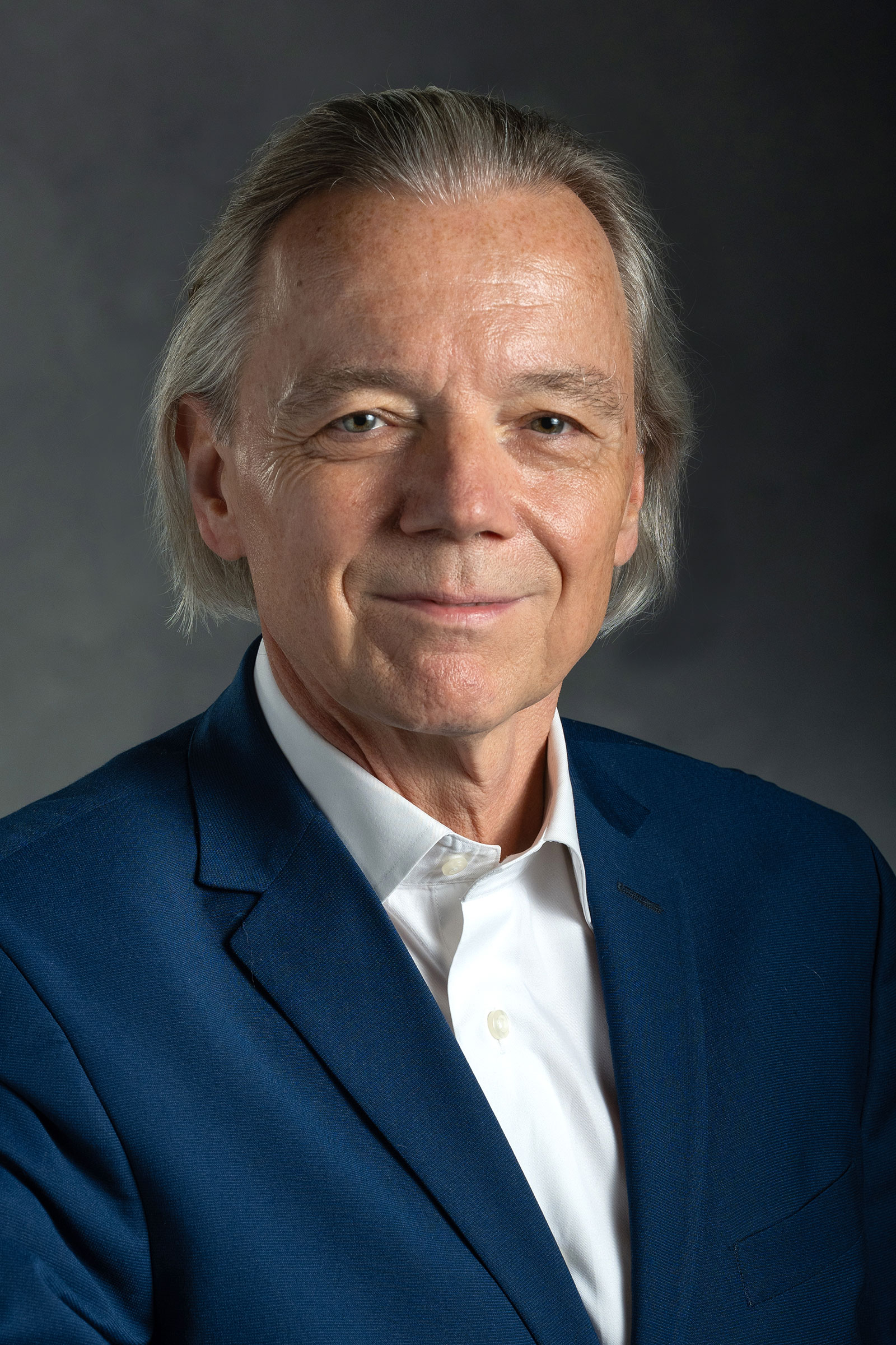 Portrait of Johannes Bauer. He is wearing a navy blue suit jacket and a white shirt. A gray background is behind him.