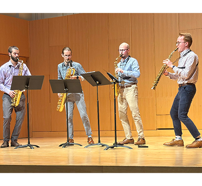 Four saxophonists perform on a stage with music stands in front of them