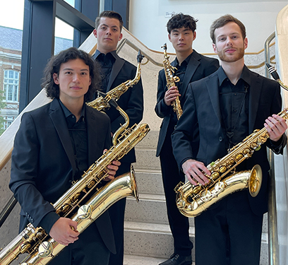 Four saxophonists pose on a stairwell holding saxophones