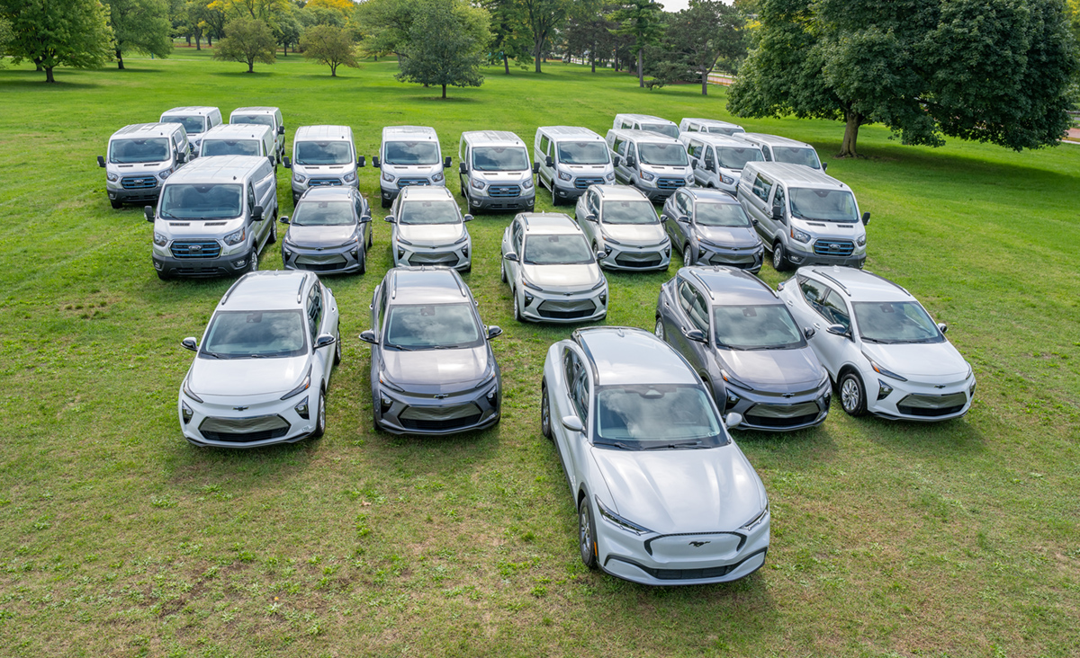 A contingent of the fleet of Michigan State University fleet of electric vehicles, including sedans, SUVs, and vans, parked on a green lawn.