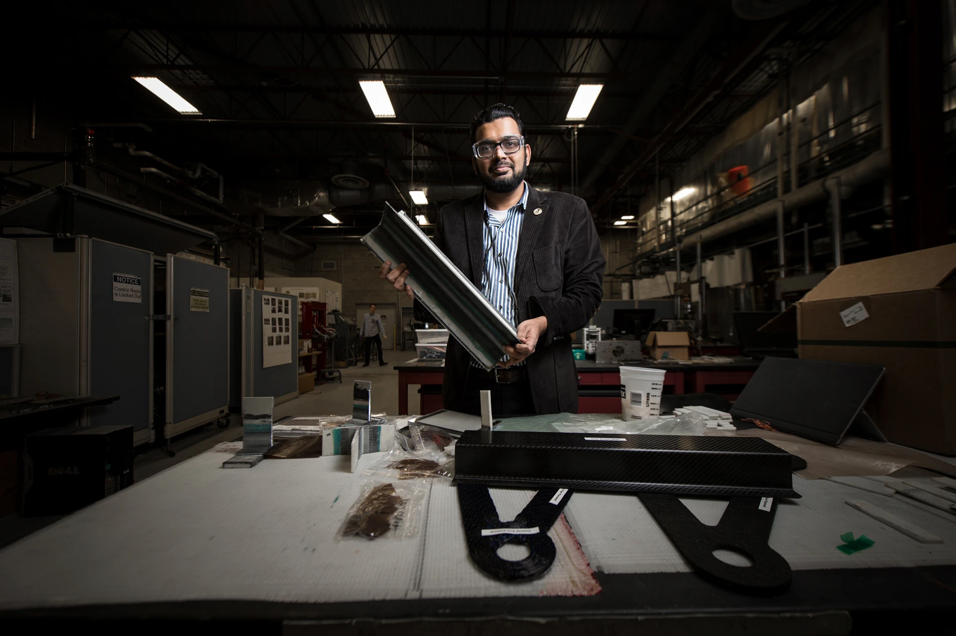 Associate Professor Mahmood Haq stands behind a table with multiple samples of composite materials on it. He’s holding one as well — a large but lightweight metal-to-composite piece about the size of his arm.