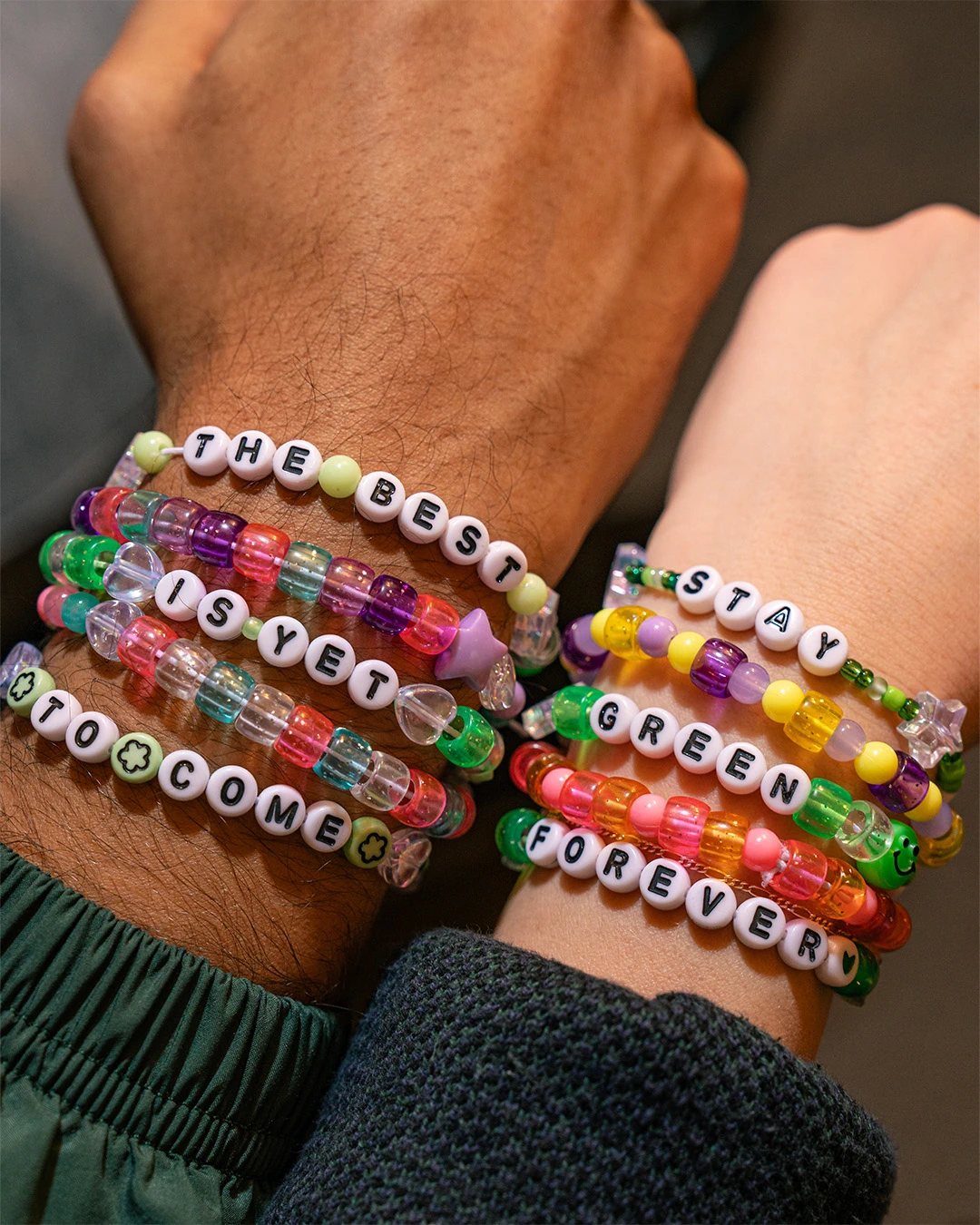 Two wrists with stacked friendship bracelets, each containing a phrase: 