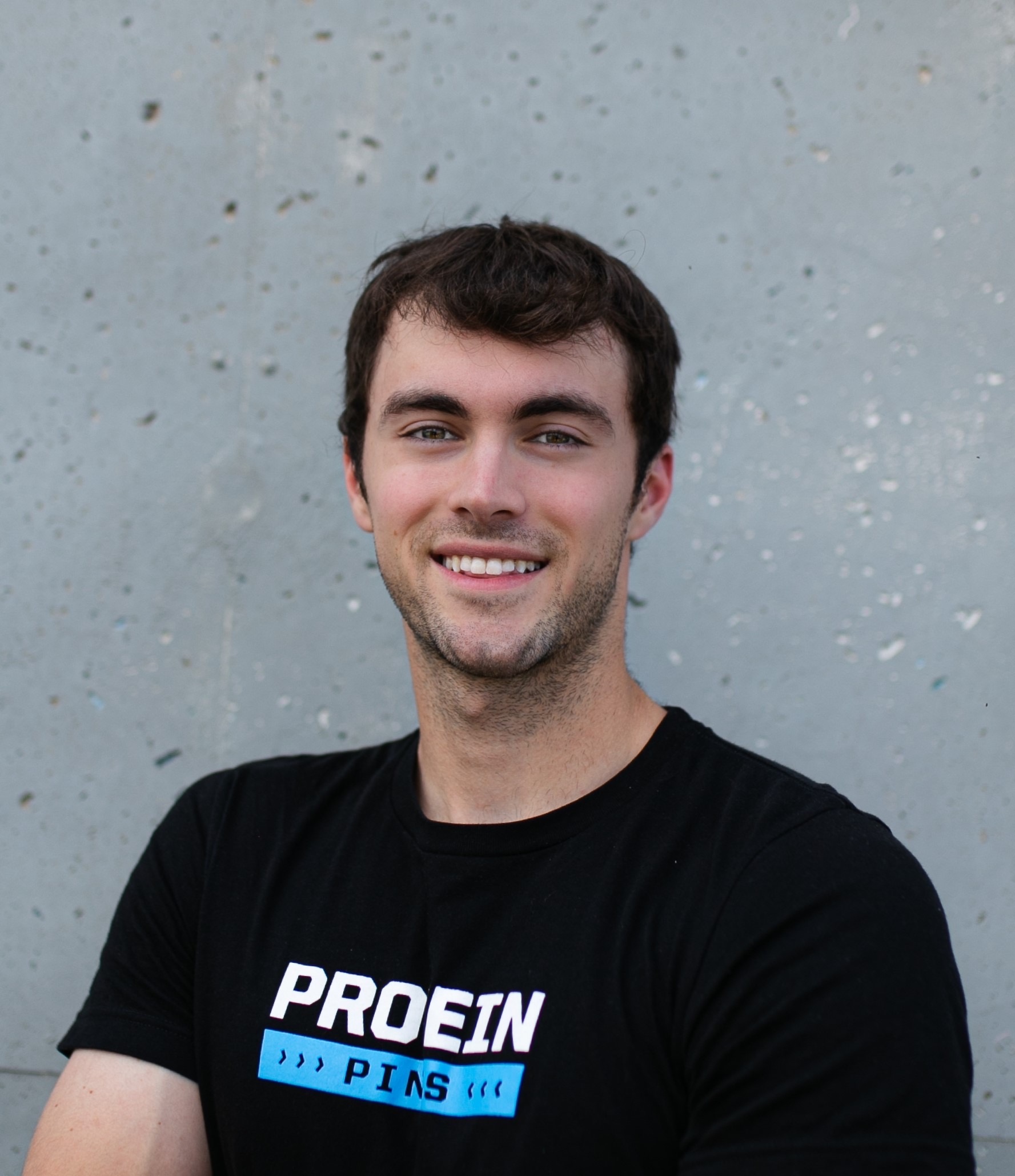Paul Riess poses in front of a wall wearing a black Protein Pints t-shirt