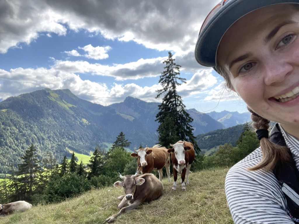 MacKenzie Jacobs takes a selfie in front of some cows and a mountain landscape in Switzerland