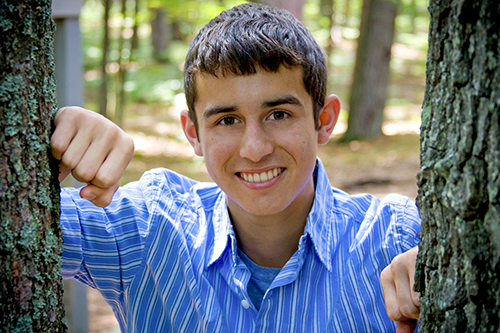 Alex Powell in a blue shirt posing between two trees.