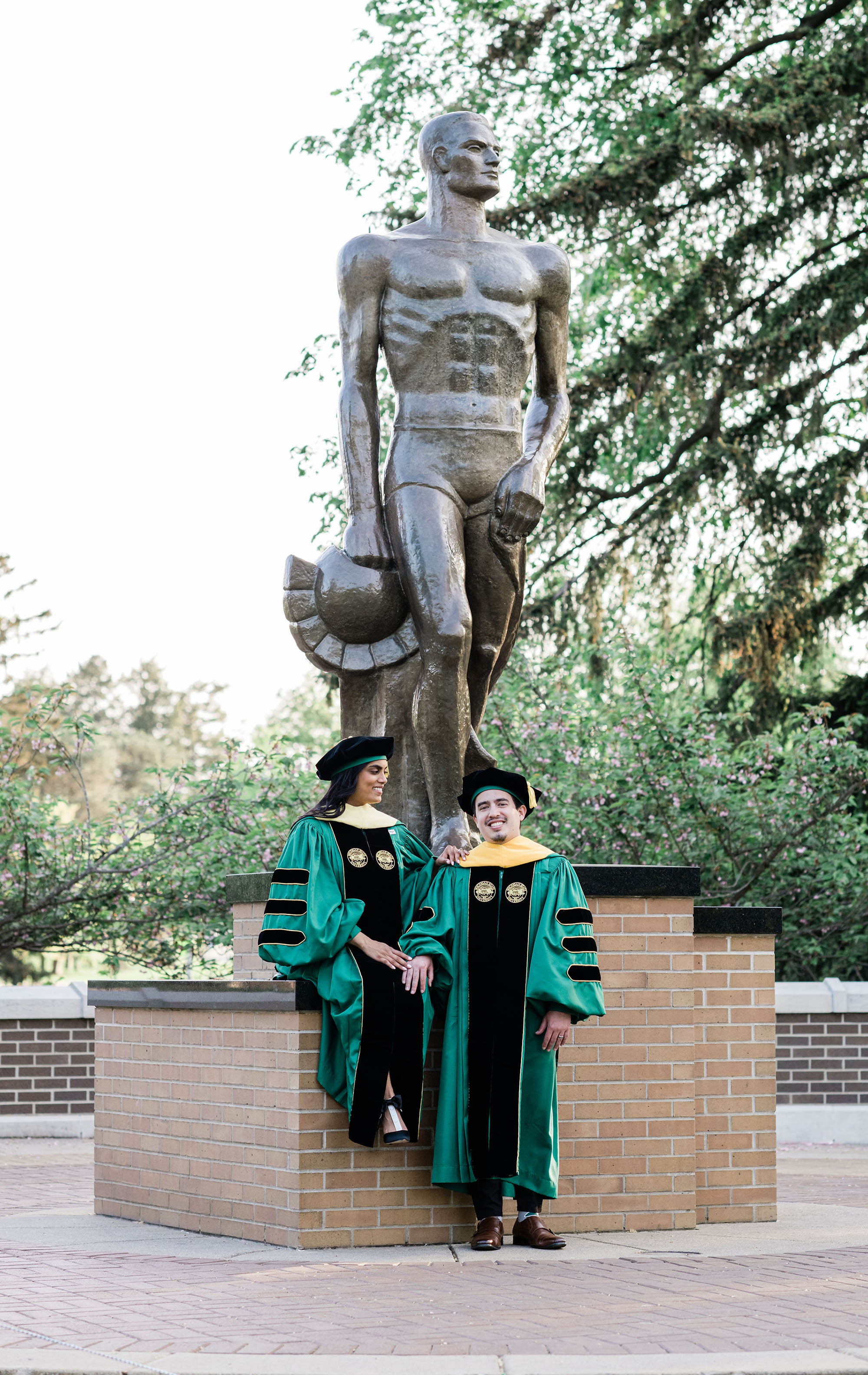 Chelsie Boodoo and husband in academic robes with Spartan statue