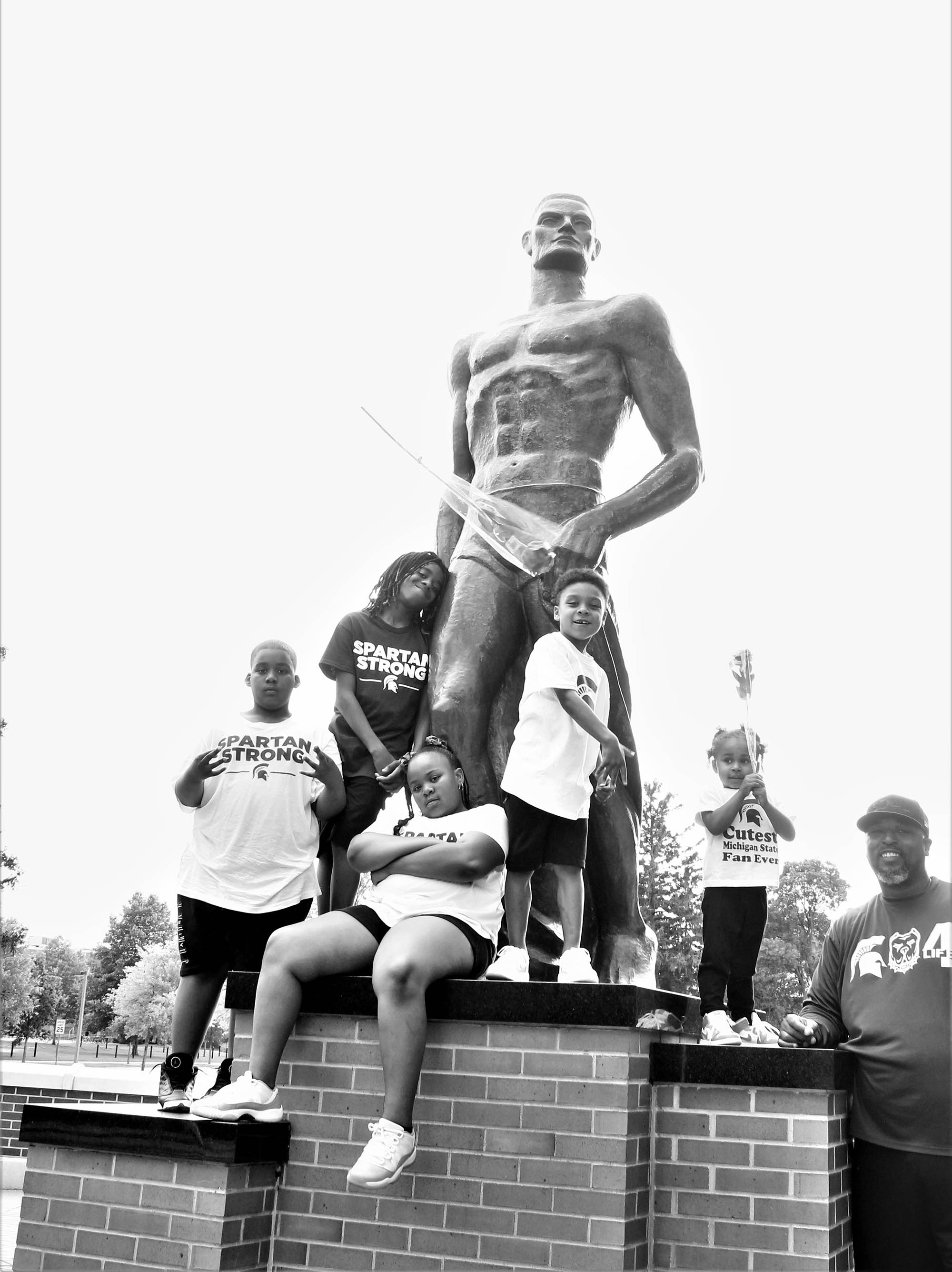 Black and white photo of Jay Greene and grandkids with Spartan statue