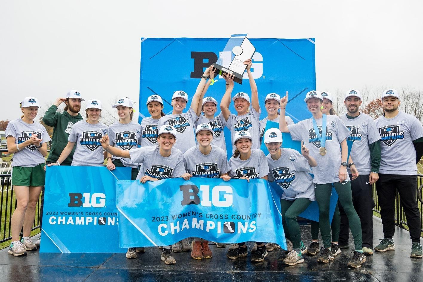 Michigan State University women's cross-country team poses while holding a trophy and a sign that reads BIG Champions