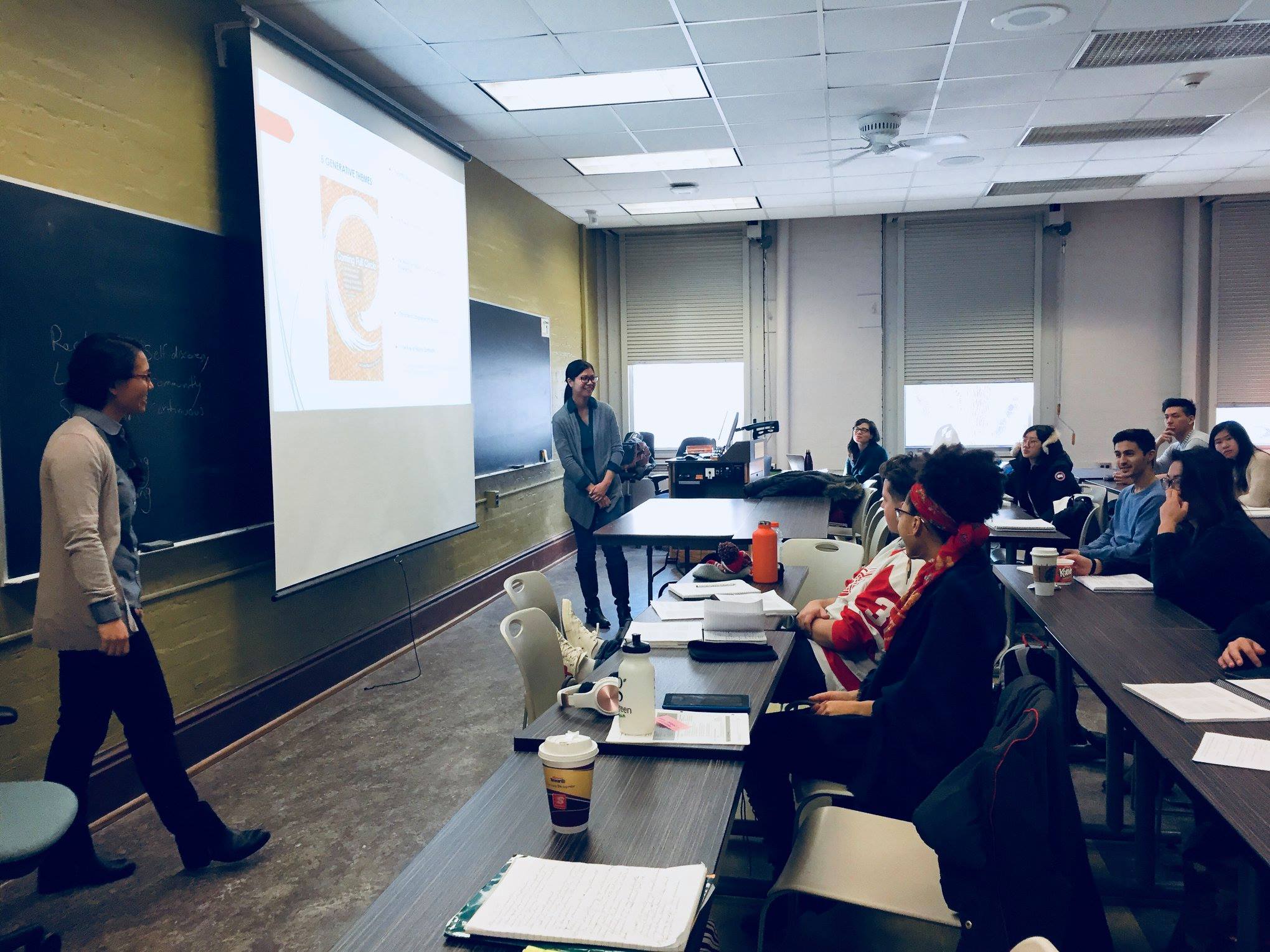 presenters standing at the front of a classroom speaking to seated students