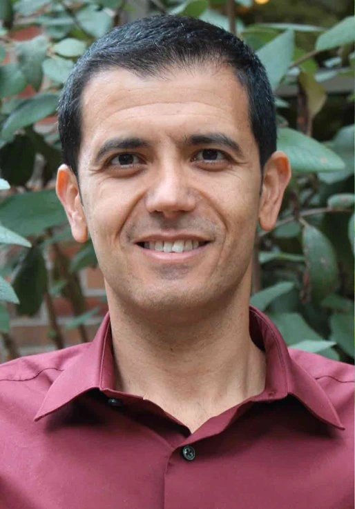 Portrait of Ehsan Ghane, an MSU researcher and specialist in sustainable agricultural engineering, smiling with a backdrop of foliage, indicative of his commitment to environmental stewardship and innovative water management research.