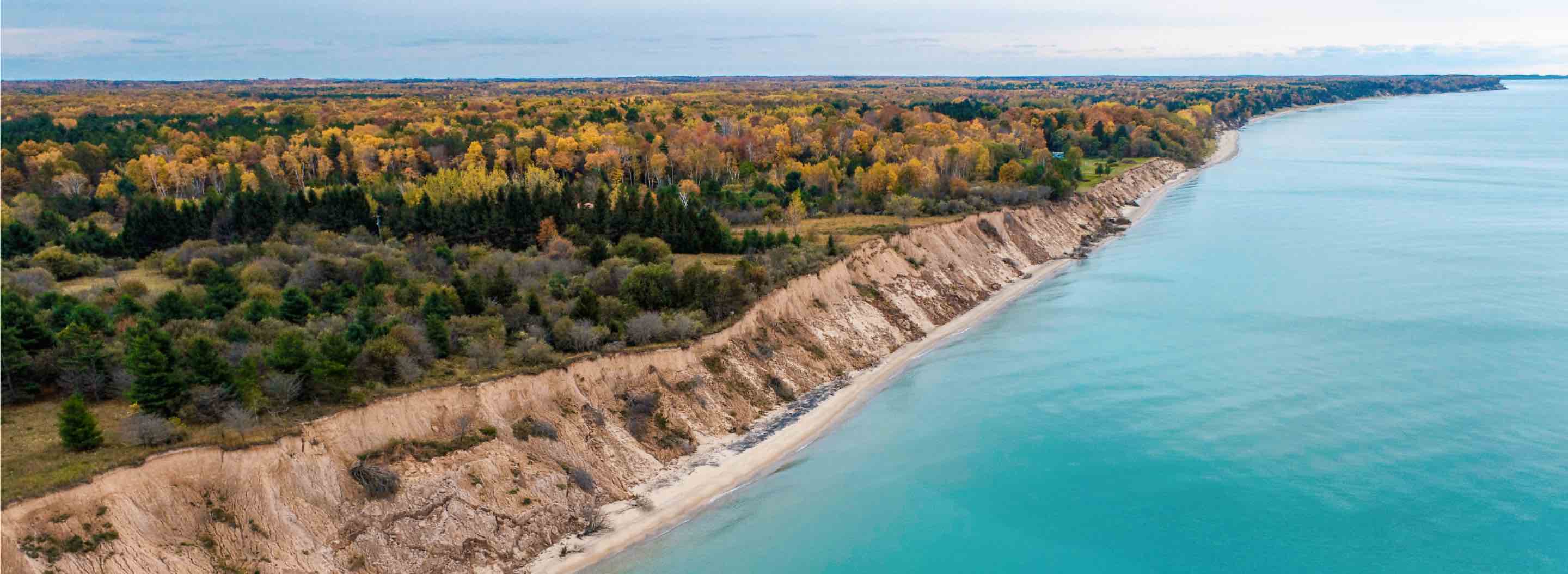 An aerial view of a Lake Michigan shoreline with dunes and trees in the background