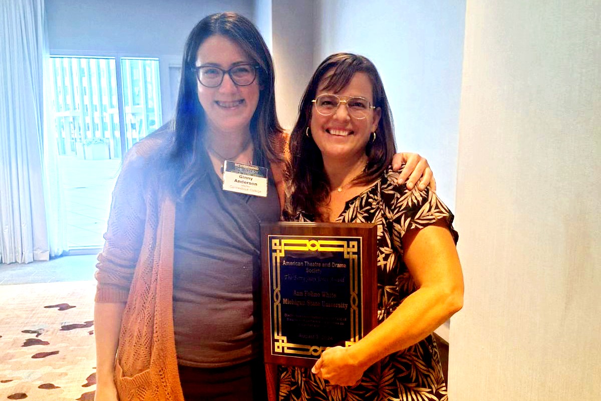Two women smile for a photo. The one on the right is holding a plaque.