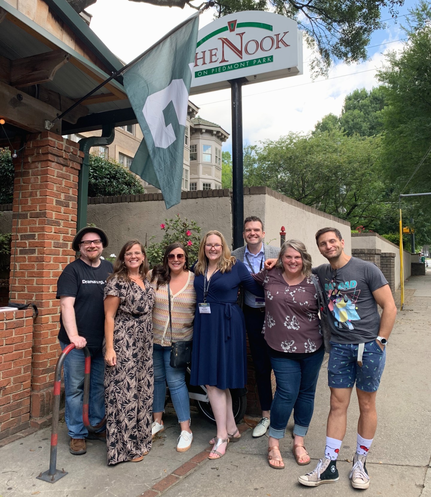 A group of people posing for a picture outside a building. A sign outside the building says “The Nook on Piedmont Park.” There is an MSU flag hanging from the building.