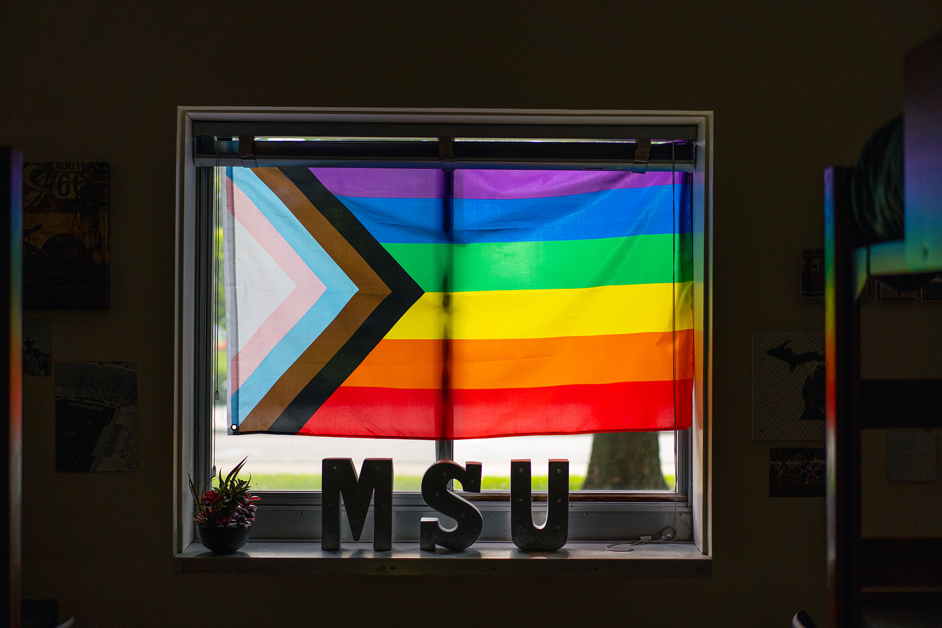 Pride progress flag in a window with MSU letter in silhouette