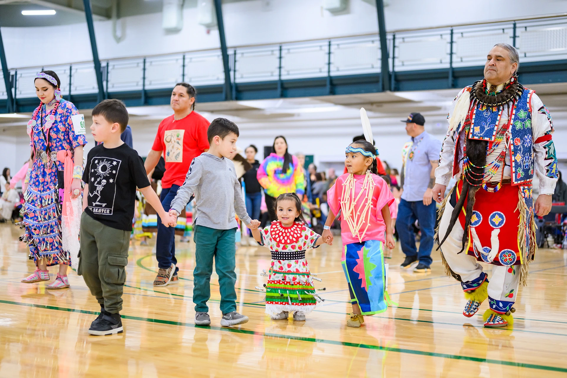 children hold hands and participate in powwow with family members