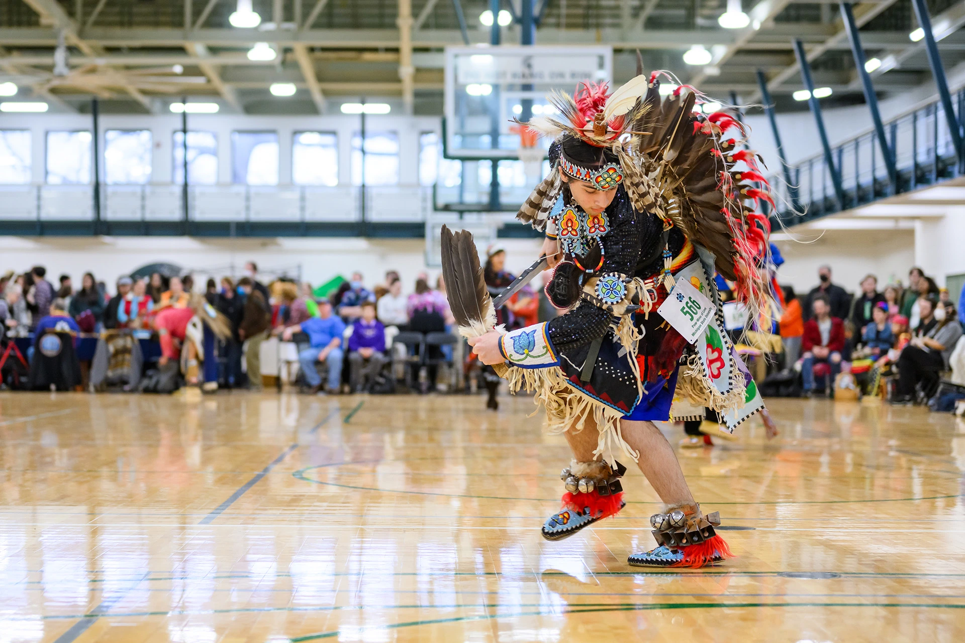 Powwow dancer cross steps facing the camera holding feathers