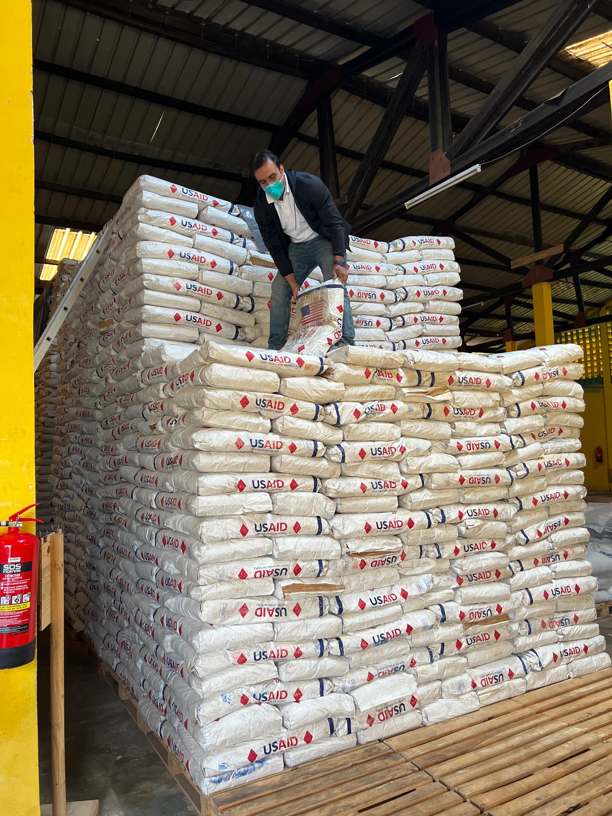 Fahim standing on top of and stacking bags of grain with USAID logo