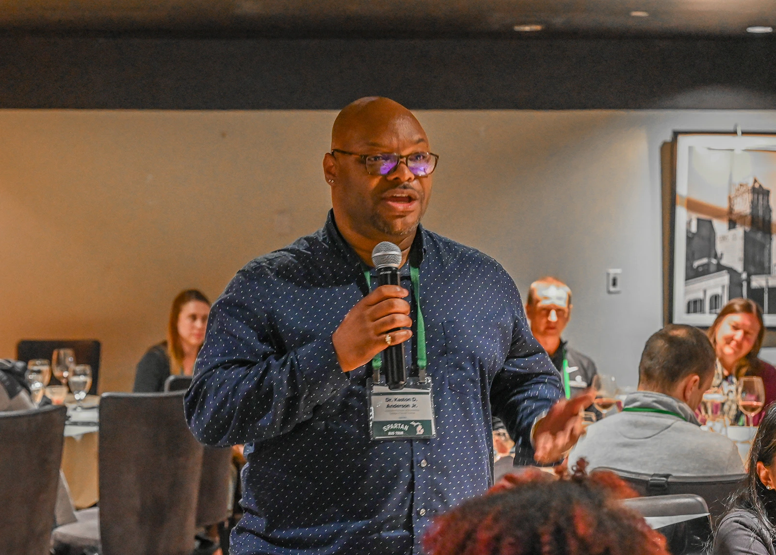 A man speaking in a microphone in a banquet room.