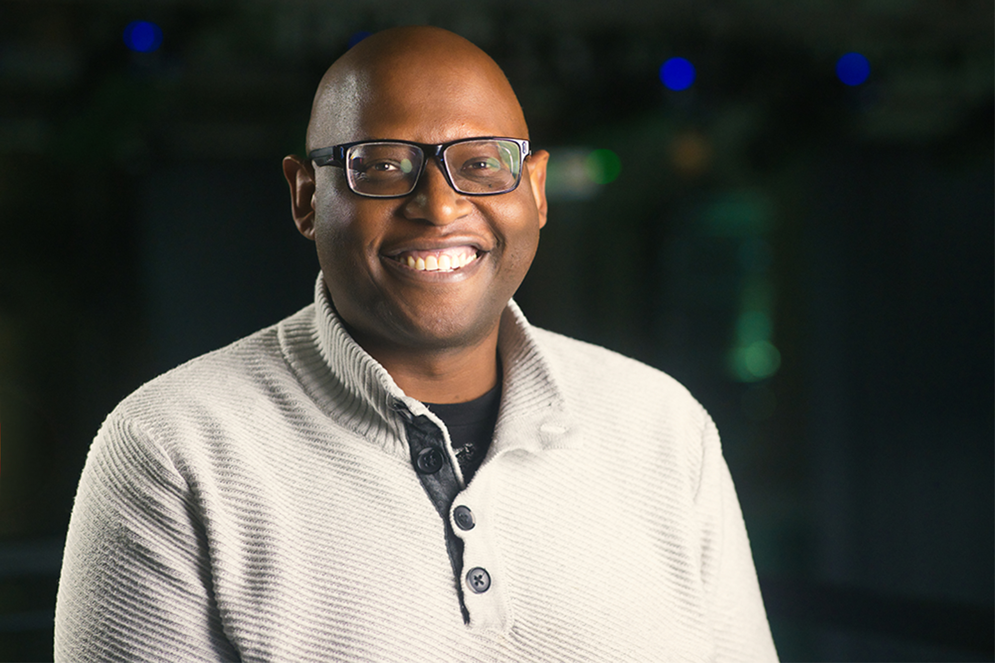 MSU Professor Julian C. Chambliss wearing glasses and a white shirt in a warehouse-style concert venue.